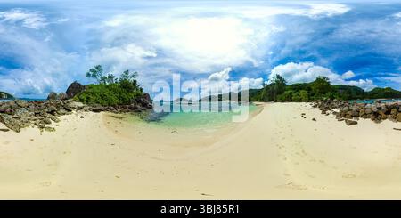 Ein ruhiger Strand mit felsigen Formationen und weichem Sand, der in klares, ruhiges Wasser mit üppigem Grün im Hintergrund führt. Port Glaud Lagune. Seychellen. VR 360. Stockfoto
