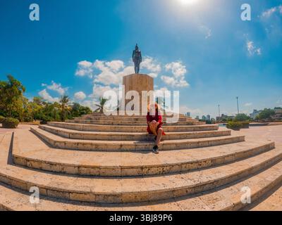 Eine Frau sitzt auf den Stufen eines Denkmals unter einem klaren blauen Himmel in Cartagena, Kolumbien, umgeben von Palmen. Stockfoto