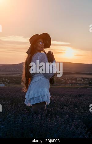 Frau in einem weißen Kleid, die bei Sonnenuntergang auf einem Lavender-Feld steht Stockfoto