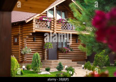 Holzblockhaus mit blumengeschmückten Balkonen, üppig grünem Garten und eleganter Landschaftsgestaltung. Friedliche ländliche Atmosphäre mit gemütlichem Naturdesign Stockfoto