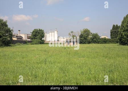 Verlassene Betonhütte auf einem Feld mit einem Industriekomplex im Hintergrund an einem sonnigen Tag in der italienischen Landschaft Stockfoto