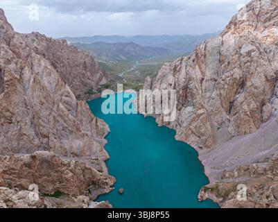 Eine große Luftaufnahme zeigt den lebhaften türkisfarbenen Kel-Suu See, der sich durch eine dramatische Bergkette mit weit entfernten Tälern schlängelt Stockfoto