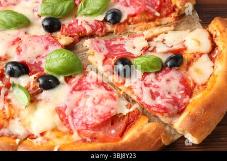 Leckere Pizza mit Salami, Käse, Basilikum und Oliven auf dem Tisch, Nahaufnahme Stockfoto