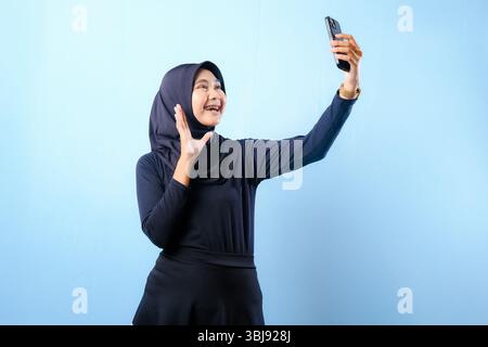 Eine Frau, die einen schwarzen Hijab trägt, macht ein Selfie mit ihrem Handy. Sie lächelt und ist glücklich Stockfoto