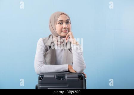 Eine Frau mit Kopftuch sitzt auf einem Koffer. Sie lächelt und sieht in die Kamera Stockfoto