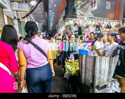 Thailand-07 April 2024-viele Leute stöbern und kaufen Waren auf einem Outdoor-Markt, mit dem Baiyoke Sky Hotel, das in das Sonnenlicht dahinter thront. Stockfoto