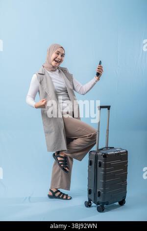 Eine Frau steht neben einem Koffer und lächelt. Sie hält ein Handy in der Hand Stockfoto