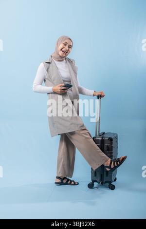 Eine Frau, die einen Schal trägt und ein Handy hält, steht neben einem Koffer. Sie ist glücklich und begeistert über ihre bevorstehende Reise Stockfoto