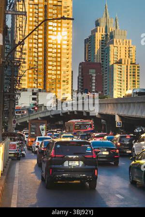Bangkok, Thailand-07. April 2024-später Nachmittag, Sonnenlicht aus niedrigem Winkel reflektiert zufällig auf Hochhäuser und stark frequentierten Verkehr darunter während der Hauptverkehrszeit. Stockfoto