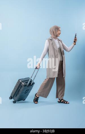 Eine Frau läuft mit einem Koffer und lächelt. Sie hält ein Handy in der Hand und macht ein Selfie. Reise- und Abenteuerkonzept Stockfoto