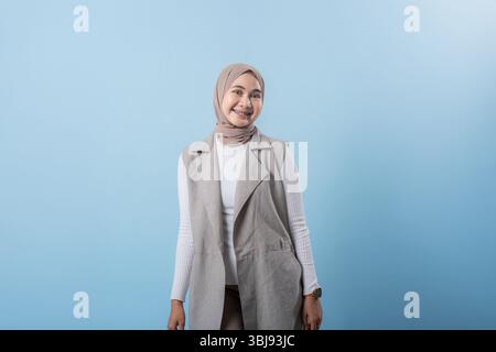 Eine Frau mit weißem Hemd und braunem Schal steht vor einer blauen Wand. Sie hat ein Lächeln im Gesicht und ist glücklich Stockfoto