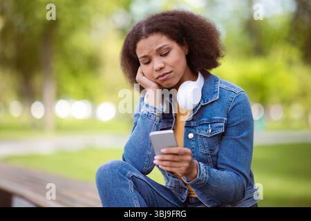Nachdenkliche afroamerikanische Studentin im Freien, die besorgt auf das Smartphone schaut Stockfoto