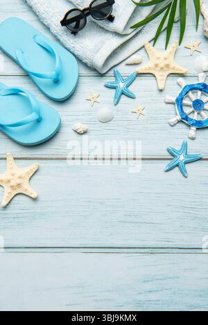 Flip flops, sunglasses, towel, seashells, starfish and ship's wheel creating a frame on a light blue wooden background with copy space Stockfoto
