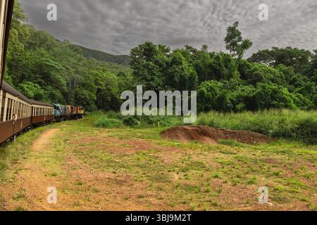 Der historische Zug fährt durch üppigen tropischen Regenwald nach Kuranda, Australien, unter einer dramatischen bewölkten Landschaft Stockfoto