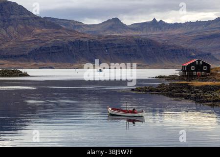 Kleines Boot und schwarzes Holzhaus, Djupivogur, Eastfjords, Island. Landschaft im Herbst mit Berghintergrund aufgenommen. Stockfoto