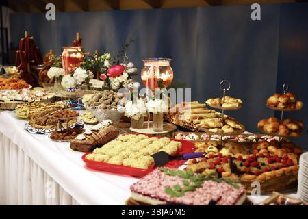Üppig dekorierter Nachtisch-Buffet-Tisch mit einer Auswahl an Gebäck, Keksen, Kuchen und Süßigkeiten, wunderschön eingerichtet mit Blumendekor. Stockfoto