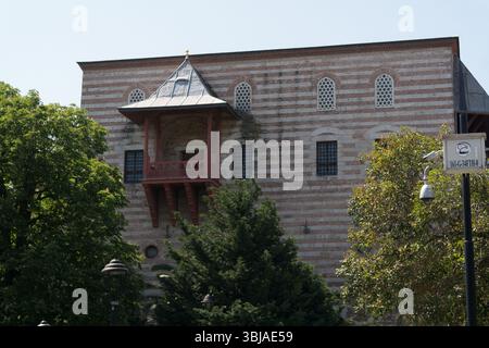 Besucher bewundern die einzigartigen architektonischen Merkmale eines historischen Gebäudes in Istanbul, umgeben von Bäumen und im Sonnenlicht getaucht. Stockfoto