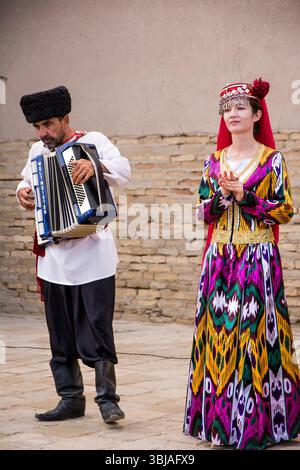 Chiwa, Usbekistan – 11. Juli 2024: Traditionelle usbekische Volksaufführung im historischen Zentrum von Chiwa. Eine Frau in bunten Nationalkleidern singt in einen Stockfoto