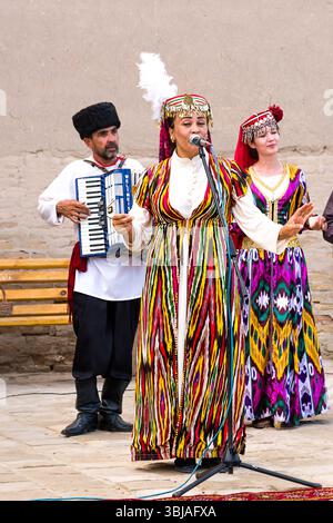 Chiwa, Usbekistan – 11. Juli 2024: Traditionelle usbekische Volksaufführung im historischen Zentrum von Chiwa. Eine Frau in bunten Nationalkleidern singt in einen Stockfoto