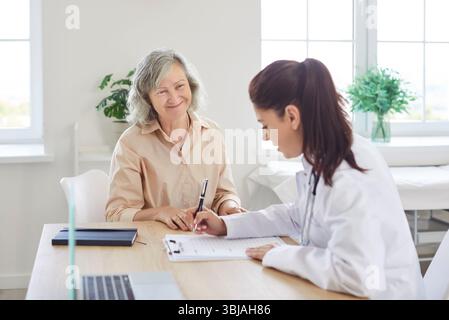 Der Arzt schreibt ein Rezept für ihre glückliche, lächelnde Seniorin aus Stockfoto