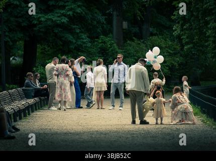 Elegant gekleidete Personen versammeln sich und machen Fotos während einer Party in einem öffentlichen Park im Sommer mit weißen Ballons Stockfoto