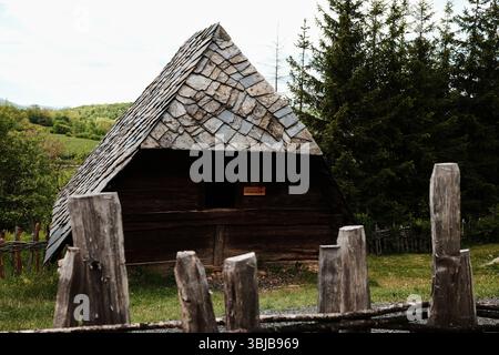 Rustikale Holzhütte mit Steindach im Ethnodorf, umgeben von Grün in Serbien. Freilichtmuseum Staro Selo. Stockfoto