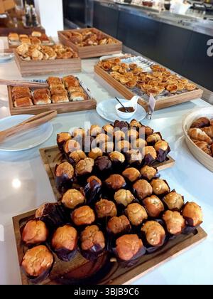 Elegantes Hotelfrühstück mit einer Auswahl an frisch gebackenen Waren, darunter Muffins Croissants und Mini-Gebäck auf einem weißen Buffettisch Stockfoto