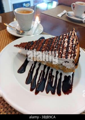 Dekadente Scheibe Schokoladendessert mit cremigen Schichten und Schokoladennebel, gepaart mit heißem Espresso auf einer weißen Platte Stockfoto