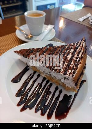 Dekadente Scheibe Schokoladendessert mit cremigen Schichten und Schokoladennebel, gepaart mit heißem Espresso auf einer weißen Platte Stockfoto