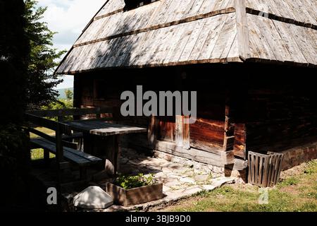 Rustikales Holzhaus mit Steinfuß und Sitzgelegenheiten im Freien in einem serbischen Ethnodorf. Freilichtmuseum Staro Selo. Stockfoto