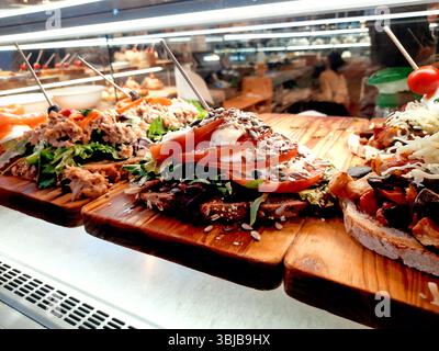 Verschiedene offene Sandwiches mit Zutaten wie Thunfisch, Tomaten, Lachs, Käse und Samen auf rustikalem Brot, auf Holzbrettern in einem Brunnen Stockfoto
