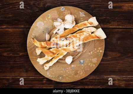 Pizzabrot mit Knoblauch auf Holzteller auf braunem Vintage Holztisch, Blick von oben. Kulinarisches Pizzastick-Essen, rustikale Stile Stockfoto