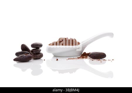 Kakaobohnen und Kakaopulver in weißer Schüssel und weißem Löffel auf weißem Hintergrund. Gesundes Superfood Stockfoto