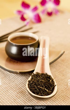 Teeblätter o einen Tee-Löffel, Tasse schwarzen Tee, herumliegen Stöcke und Blumen im Hintergrund Stockfoto