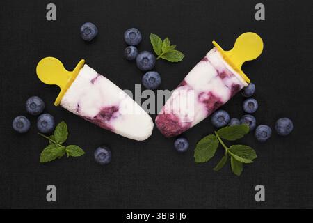 Farbenfroher Hintergrund aus Fruchteis. Zwei Eis auf schwarzem Hintergrund mit frischen Beerenfrüchten und grünen Blättern, Blick von oben. Hintergrund mit frischem Obst Stockfoto