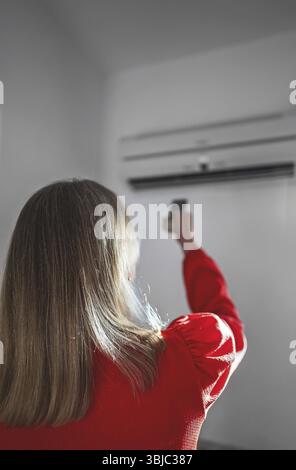 Frau mit Fernbedienung, die auf die Klimaanlage gerichtet ist Stockfoto