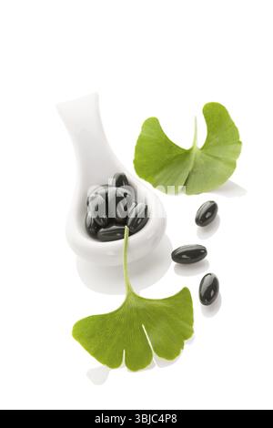 Ginkgo-Blätter mit Gelkapseln isoliert auf weißem Hintergrund mit Reflexion. Alternativmedizin, Nahrungsergänzungsmittel, Naturheilmittel Stockfoto