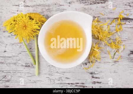 Löwenzahn-Honig-Hintergrund, Kräuterheilmittel. Löwenzahnblüte und -Stiel und Honig in der Schüssel, Draufsicht Stockfoto