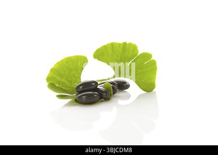 Ginkgoblätter mit Gelkapseln auf weißem Hintergrund mit Reflexion. Alternative Medizin, Nahrungsergänzungsmittel Stockfoto
