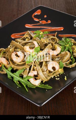Leckere Tagliatelle mit Garnelen und frischem Rucola auf schwarzem Teller garniert Stockfoto