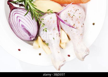 Rohe Hähnchenschenkel mit frischem Gemüse Zwiebeln, Rosmarin auf weißem Teller Nahaufnahme Stockfoto