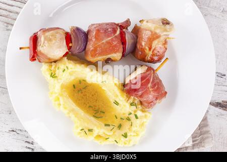 Leckerer Geflügel- und Speckkebab mit Kartoffelpüree auf weißem Teller. Kulinarische Fleischbrötchen am Spieß Stockfoto