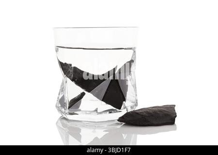 Shungitsteine in Glas Wasser isoliert auf weißem Hintergrund. Wasserreinigung, alternative Medizin Stockfoto