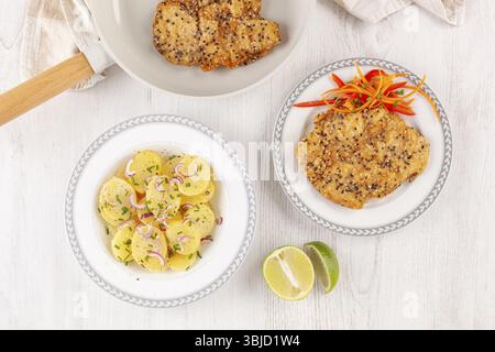 Knuspriges Weiner Schnitzel mit Sesamsamen in der Pfanne mit Kartoffelsalat von oben. Gebratenes Hühnersteak Stockfoto