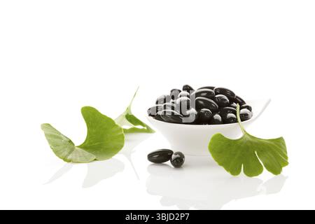 Ginkgo-Blätter mit Gelkapseln isoliert auf weißem Hintergrund mit Reflexion. Alternativmedizin, Nahrungsergänzungsmittel, Naturheilmittel Stockfoto