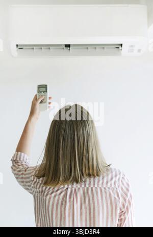Frau mit Fernbedienung, die auf die Klimaanlage gerichtet ist Stockfoto