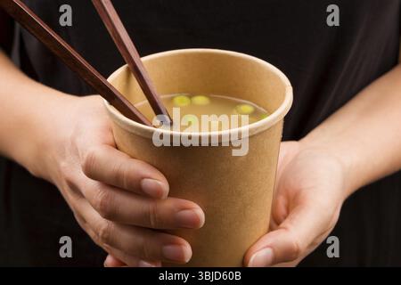 Frau isst unterwegs. Miso-Suppe in Tassen zum Mitnehmen. Traditionelle asiatische Cousine Stockfoto