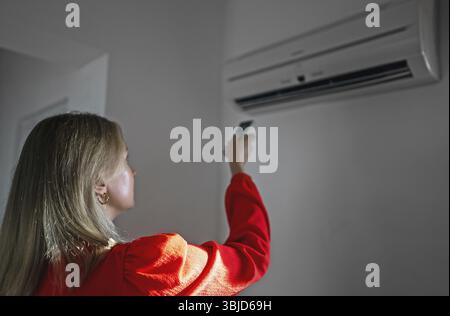 Frau mit Fernbedienung, die auf die Klimaanlage gerichtet ist Stockfoto