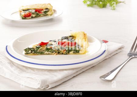 Stück Kuchen mit Spinat und Tomaten. Kulinarische vegetarische Speisen Stockfoto