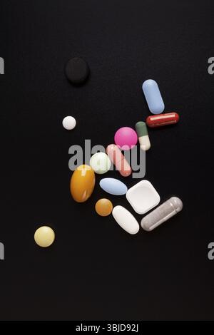 Verschiedene Tabletten, Tabletten und Kapseln für pharmazeutische Arzneimittel auf schwarzem Hintergrund von oben mit Kopierraum Stockfoto